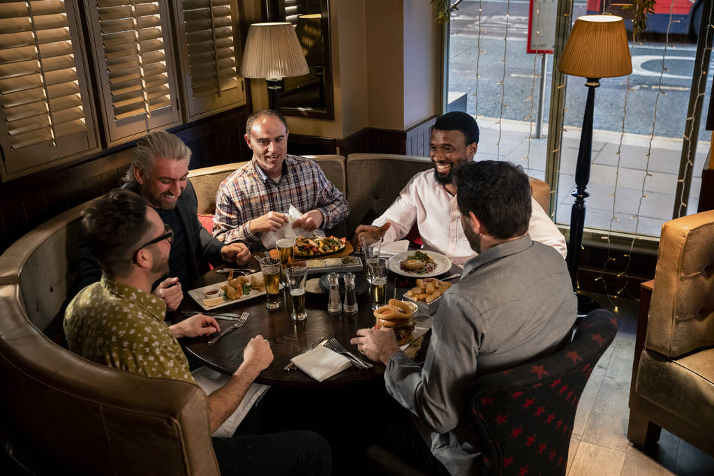 Μια ομάδα ώριμων αντρών που κάθονται στο τραπέζι σε ένα εστιατόριο. Απολαμβάνουν το φαγητό, την κουβέντα και το γέλιο.. - Φωτογραφία, εικόνα