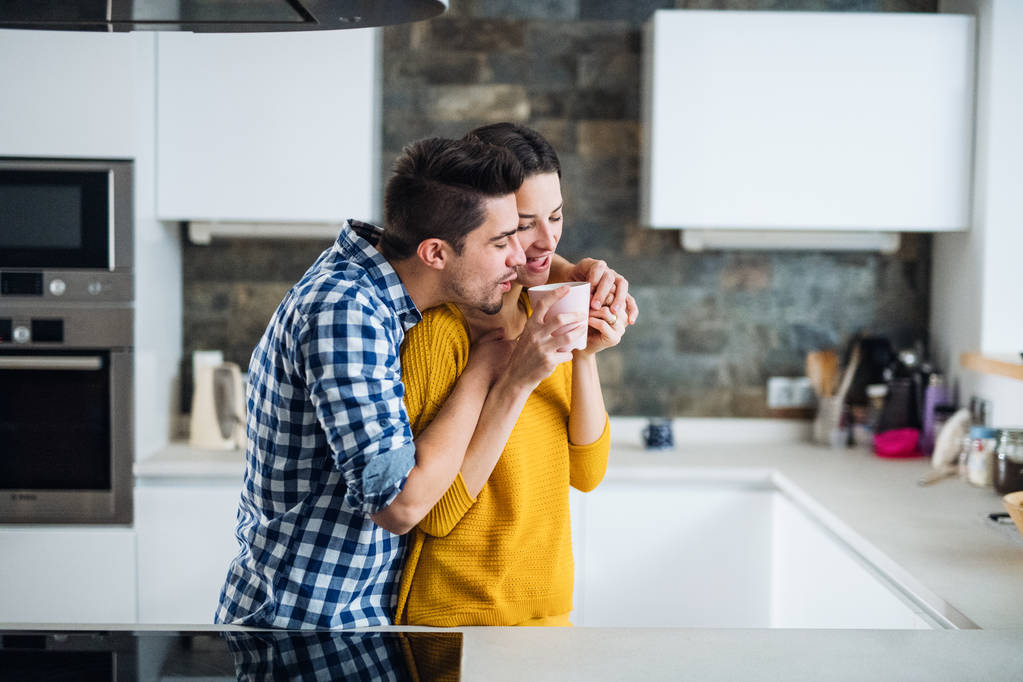 Un jeune couple debout dans une cuisine à la maison, buvant du café
. - Photo, image