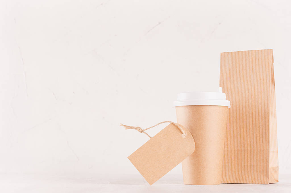 Кофе на вынос макет для бренда - коричневый бумажный стаканчик с пустой этикеткой и ремесленной сумкой на белой доске, копировальное место
. - Фото, изображение