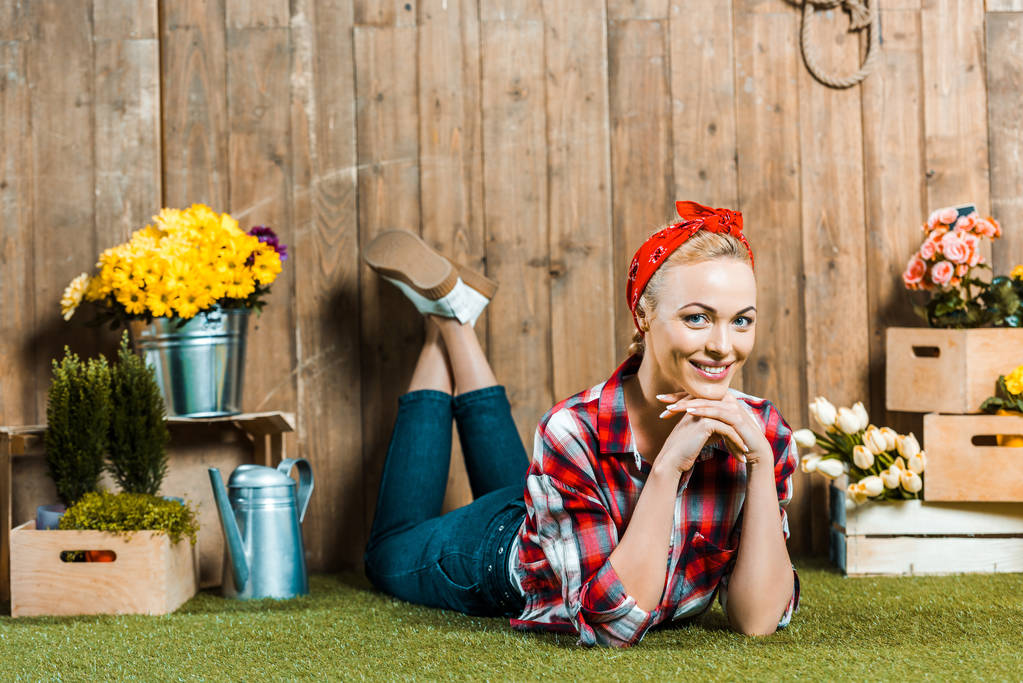 donna felice sdraiata con gambe incrociate sull'erba vicino a recinzione in legno e fiori
 - Foto, immagini