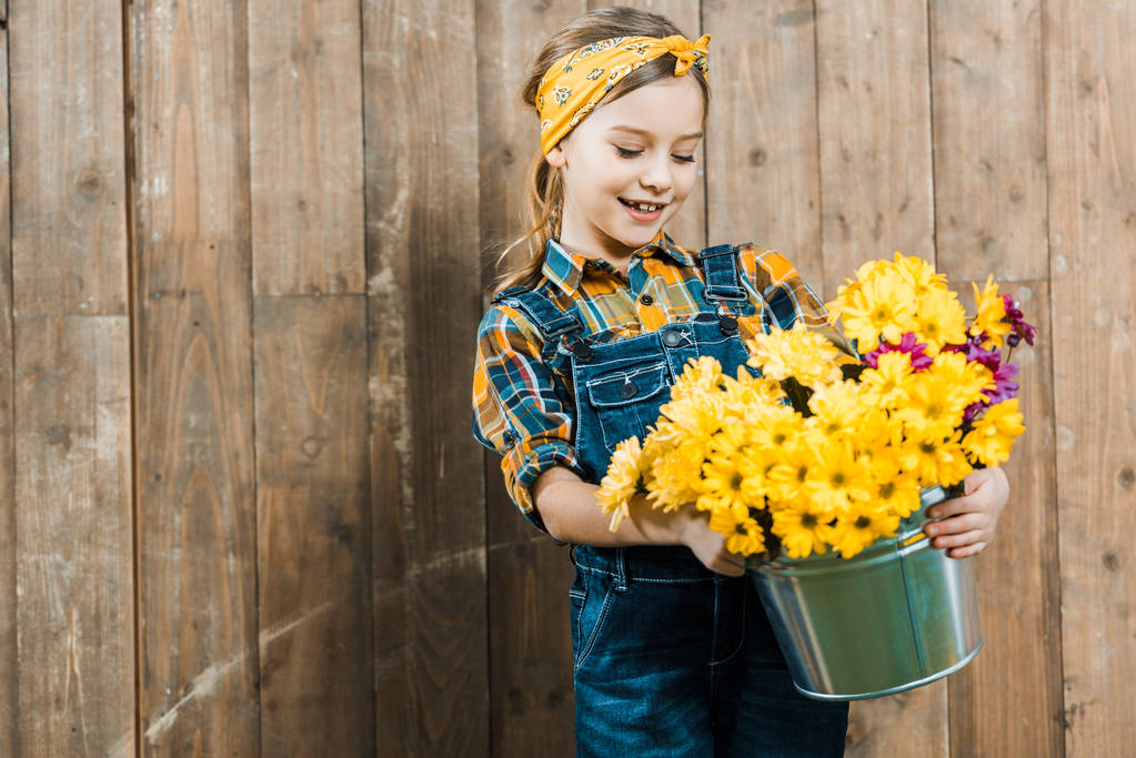 Glückliches Kind blickt auf Blumen im Eimer und steht am Holzzaun - Foto, Bild
