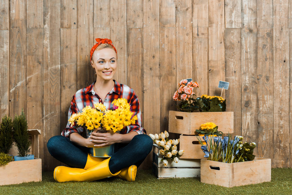 onnellinen nainen istuu ristissä jalat ja tilalla kukkia
 - Valokuva, kuva