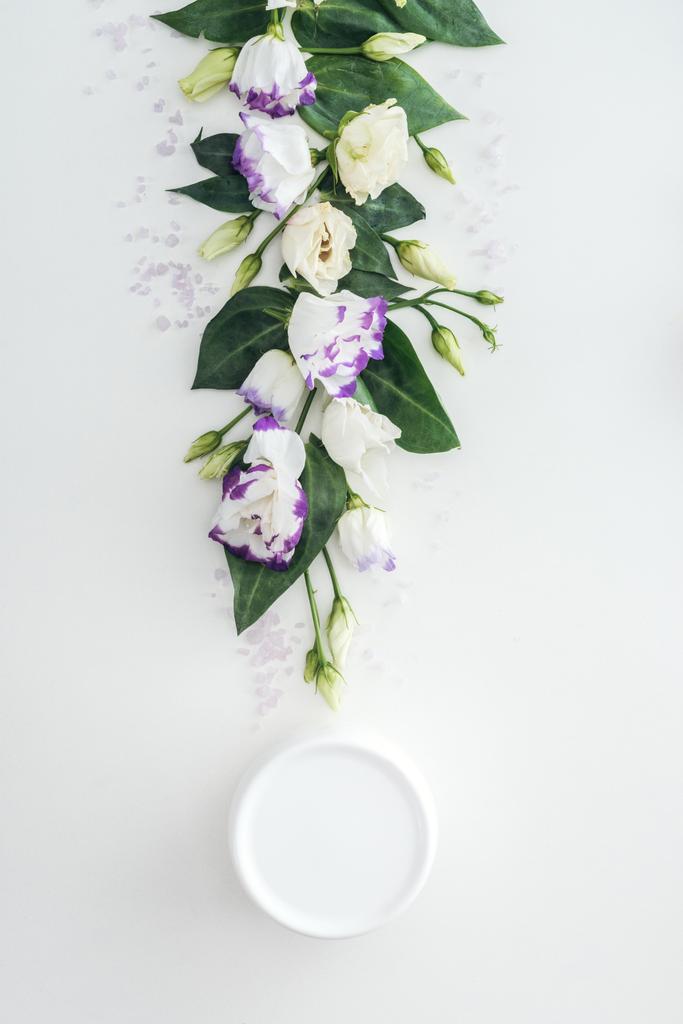 bovenaanzicht van samenstelling met paarse en witte eustoma, schoonheid room in fles op witte achtergrond - Foto, afbeelding