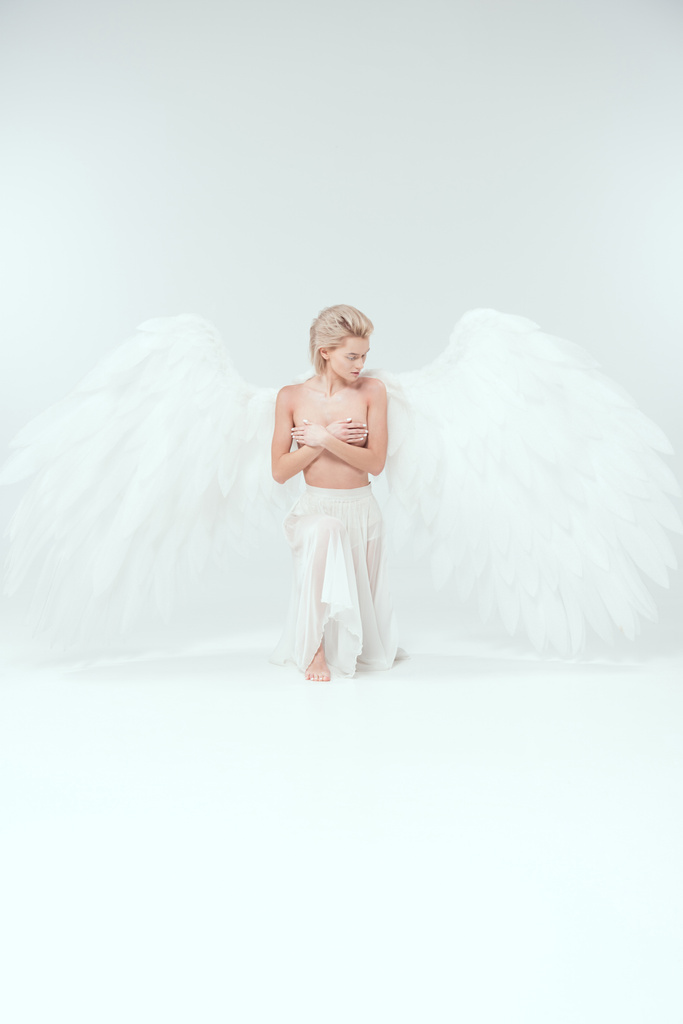 krásná mladá žena s andělskými křídly, který zakrýval ňadra při Pózování na bílém pozadí - Fotografie, Obrázek