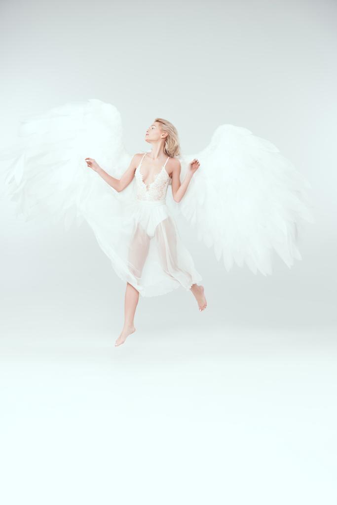 schöne Frau im Engelskostüm mit Flügeln springt isoliert auf Weiß mit Kopierraum - Foto, Bild