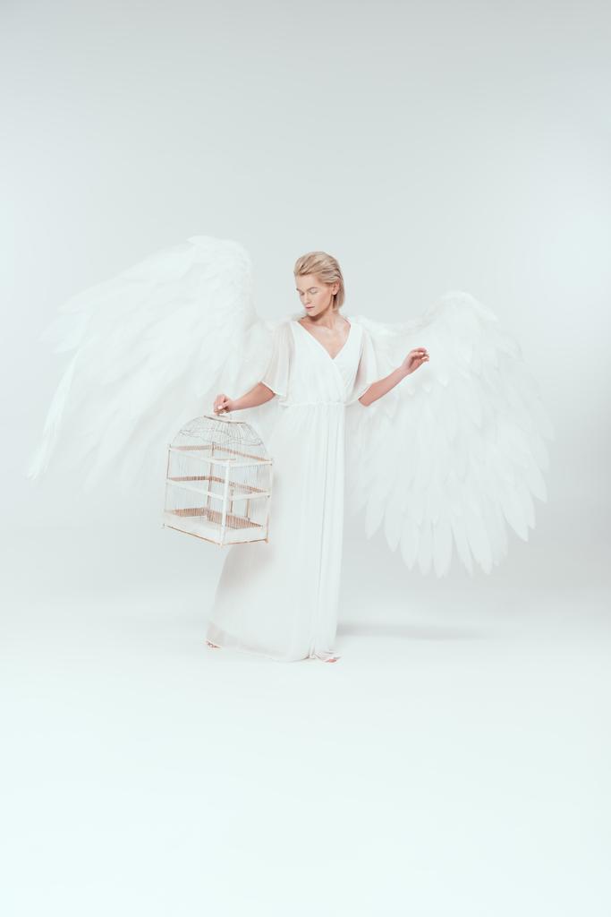 hermosa mujer en traje de ángel con alas sosteniendo jaula de pájaro aislado en blanco
 - Foto, imagen