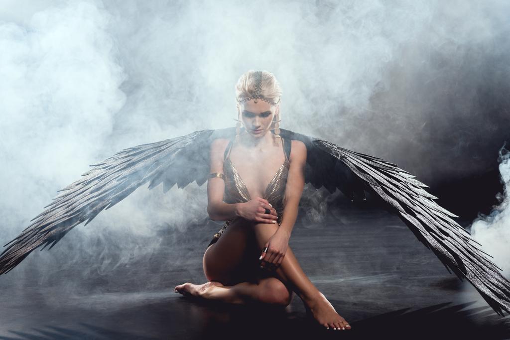 belle femme sexy avec des ailes d'ange noir assis et posant sur fond sombre
 - Photo, image