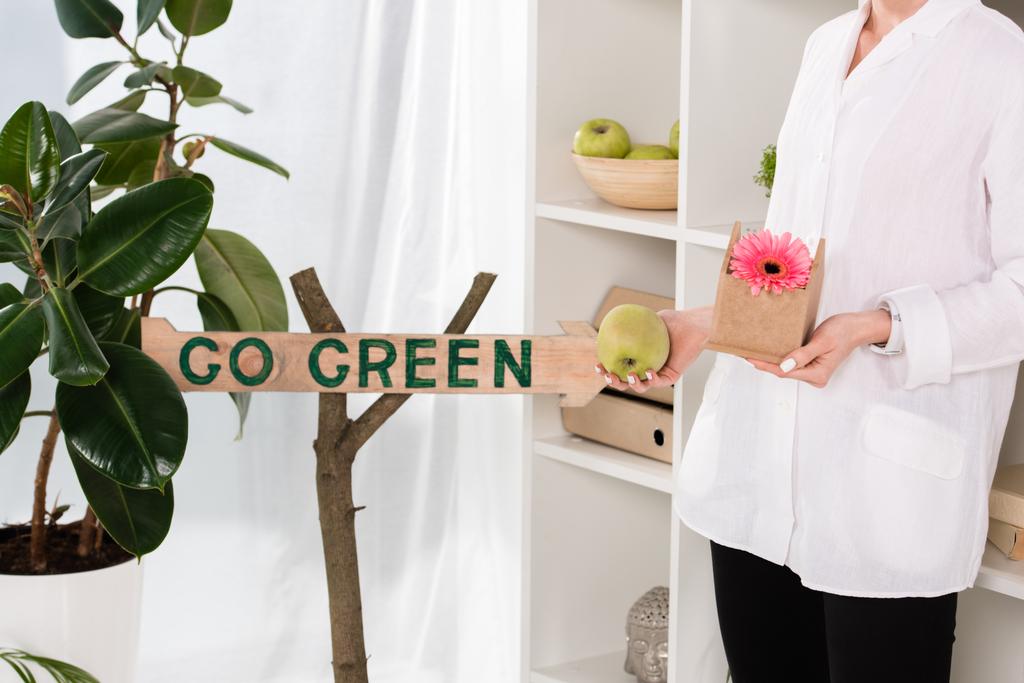 обрезанный вид на предпринимательницу, держащую небольшой картонный домик с цветком рядом идут зеленый знак в офисе, экологическая концепция
  - Фото, изображение