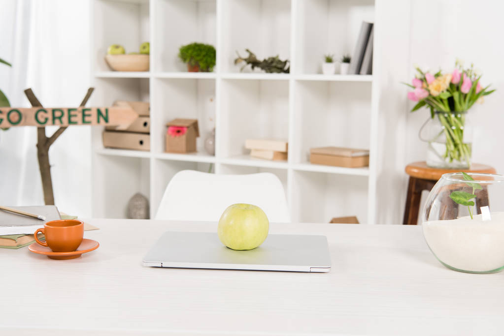 espacio de trabajo con manzana en el ordenador portátil cerca ir letrero verde en la oficina moderna, concepto de ahorro ambiental
  - Foto, imagen