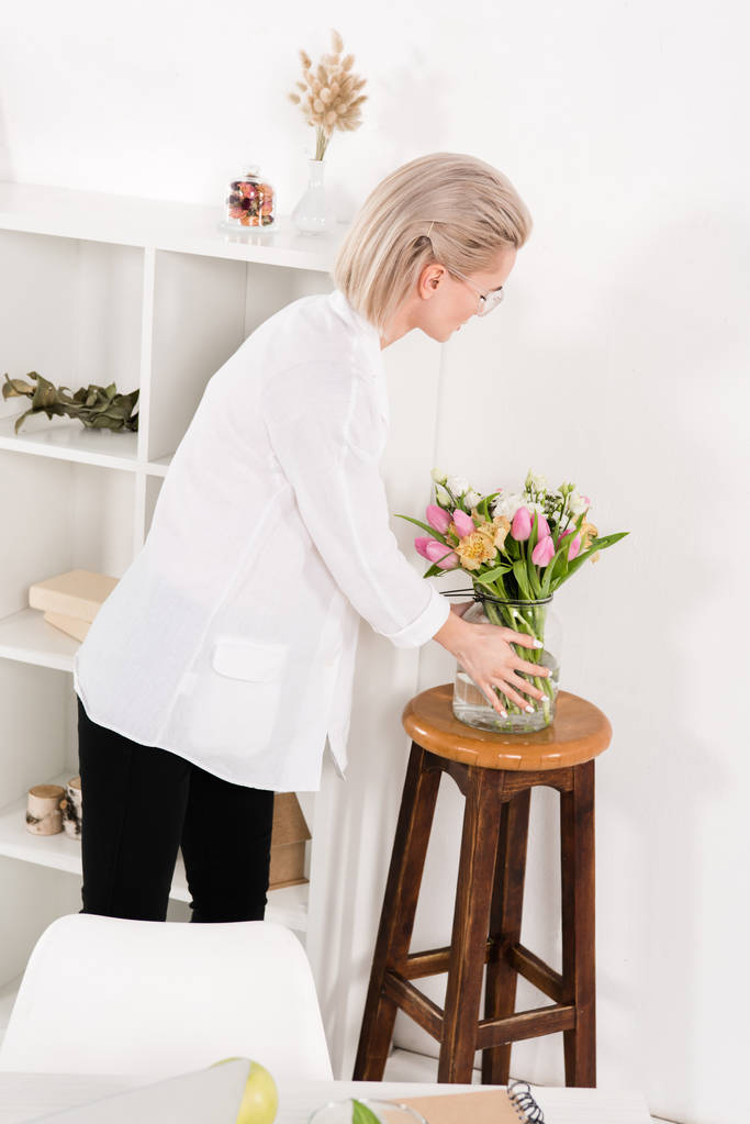  vrouw kijken naar bloemen in vaas in moderne kantoren - Foto, afbeelding