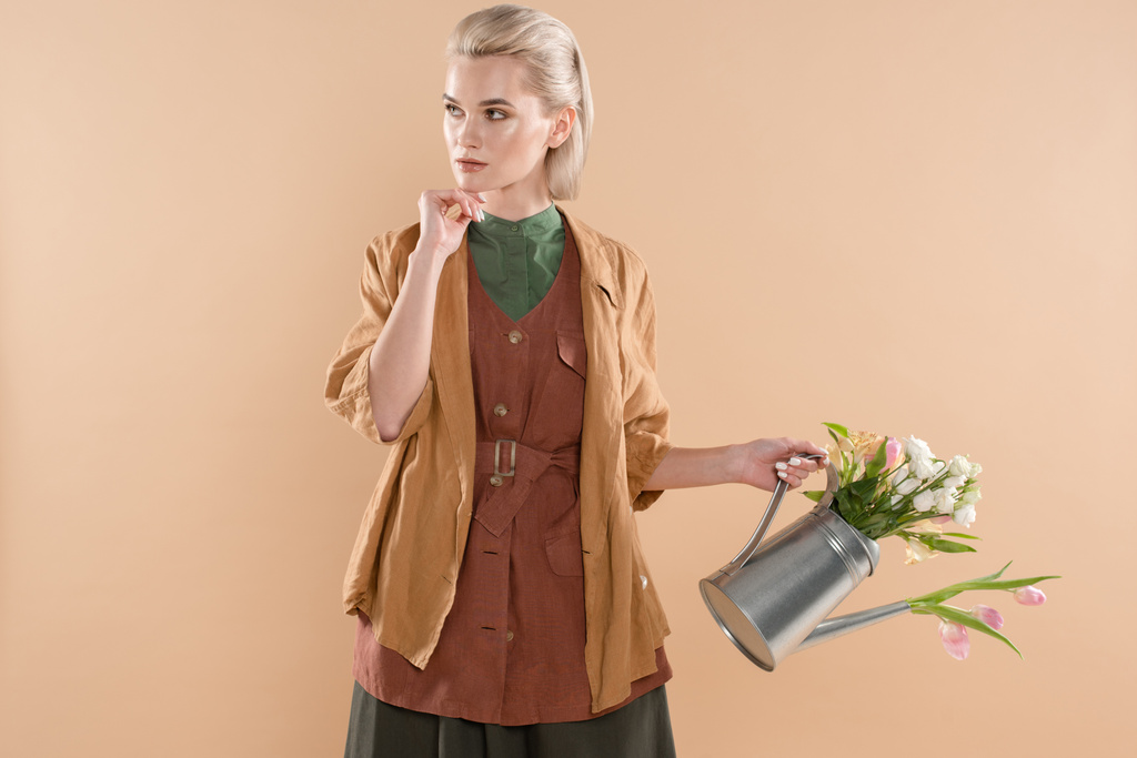 chica pensativa en ropa ecológica sosteniendo regadera con flores aisladas sobre fondo beige, concepto de ahorro ambiental
 - Foto, imagen