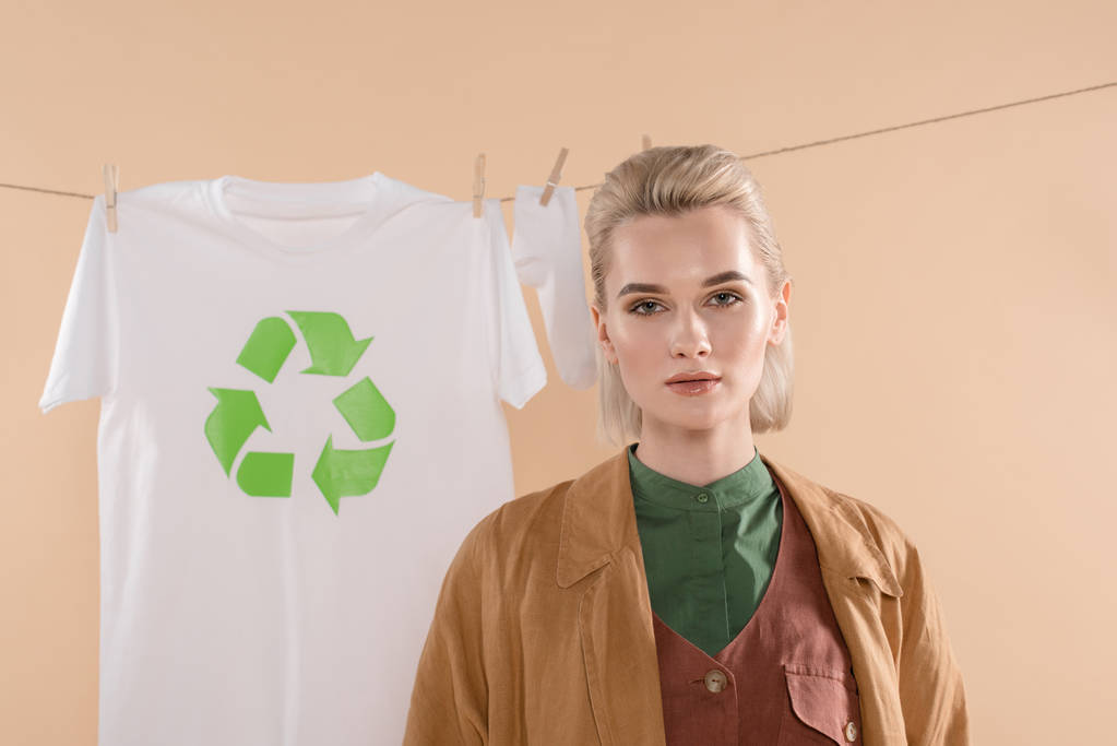 Selektywny fokus blond kobiety stojącej w pobliżu skarpetki i t-shirt z recyklingu znak na clothesline na białym tle na beż, środowiska zapisywanie koncepcja - Zdjęcie, obraz