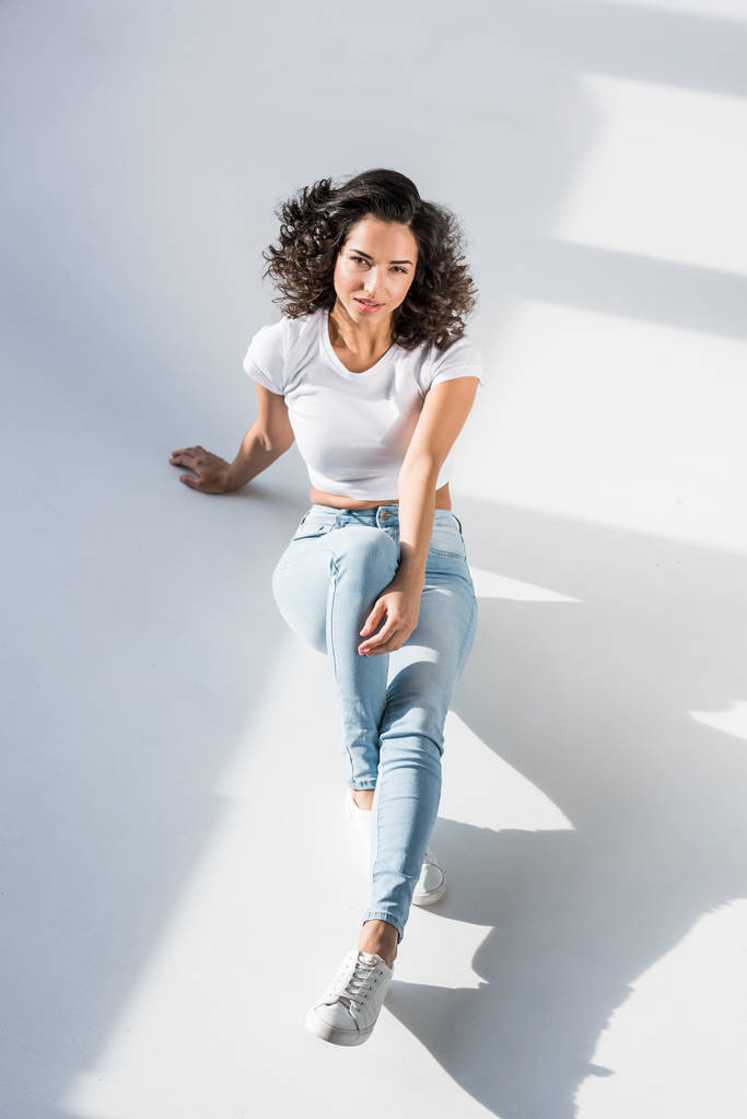 Zvědavá mladá žena v džíny sedí na podlaze - Fotografie, Obrázek