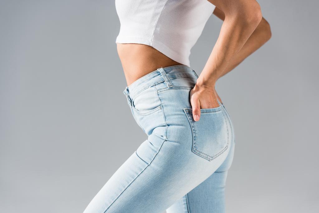Schnappschuss von sexy Mädchen in Jeans mit Händen in Taschen isoliert auf grau - Foto, Bild