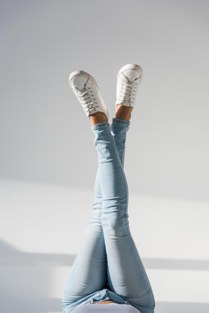 Cropped view of woman in blue jeans posing with crossed legs on grey background - Photo, Image