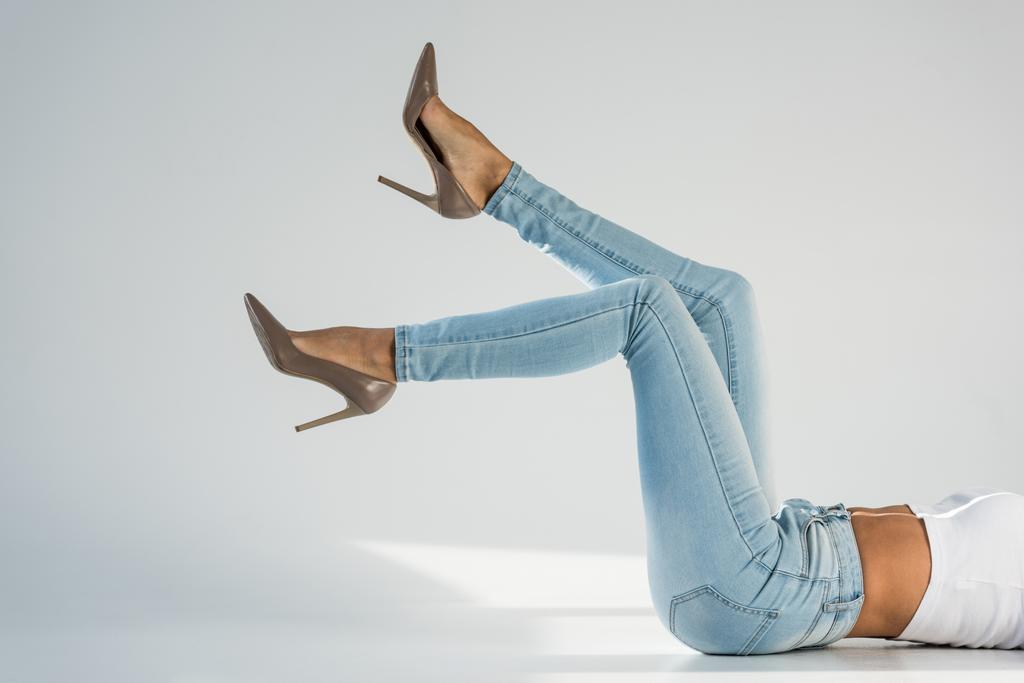 Vista parcial de mulher jovem em jeans e sapatos de salto alto em fundo cinza
 - Foto, Imagem