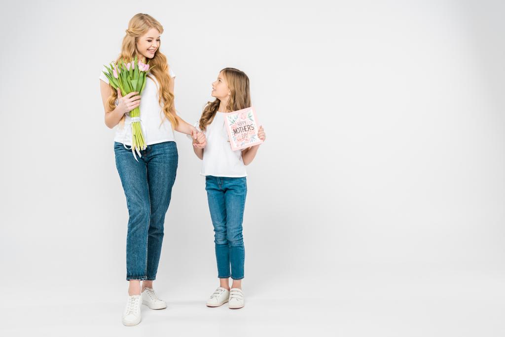happy mother with beautiful pink tulips, and smiling daughter with happy mothers day greeting card holding hands on white background - Photo, Image