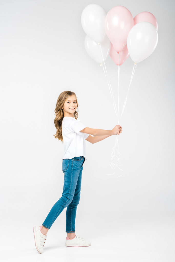 милый улыбающийся ребенок держит праздничные белые и розовые воздушные шары на белом фоне
 - Фото, изображение