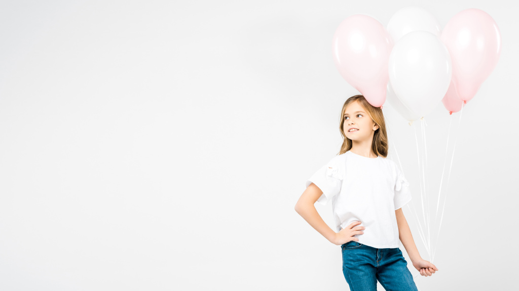niño sonriente con la mano en la cadera sosteniendo globos de aire festivos de color rosa y blanco sobre fondo blanco con espacio para copiar
 - Foto, Imagen