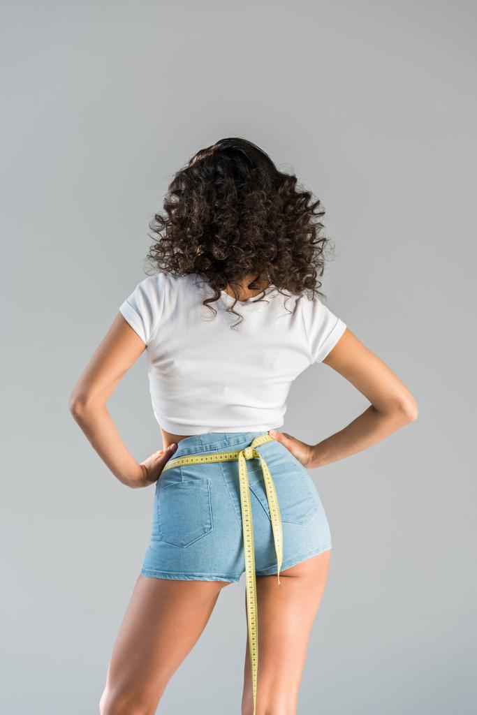 Back view of confident woman in shorts with measuring tape isolated on grey - Photo, Image