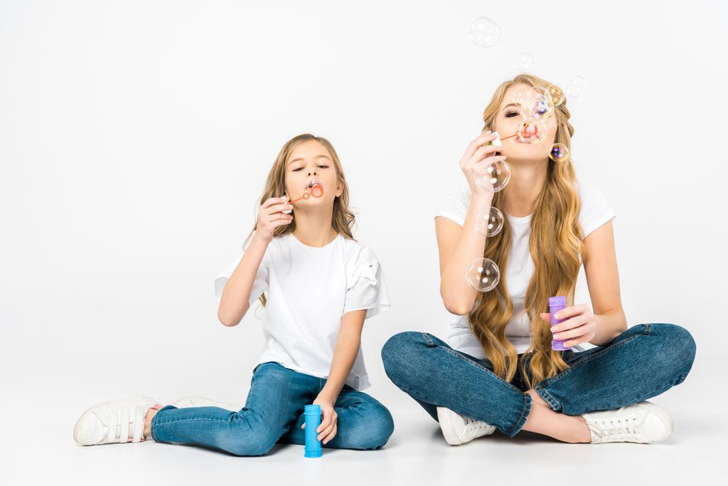 lindo niño con bonita madre soplando burbujas de jabón mientras está sentado en el suelo sobre fondo blanco
 - Foto, imagen
