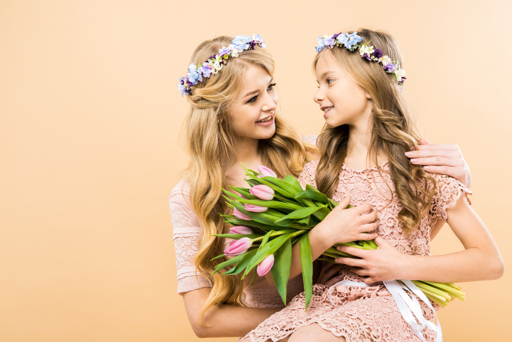lachende dochter met boeket van roze tulpen zittend op moeders knieën op gele achtergrond - Foto, afbeelding
