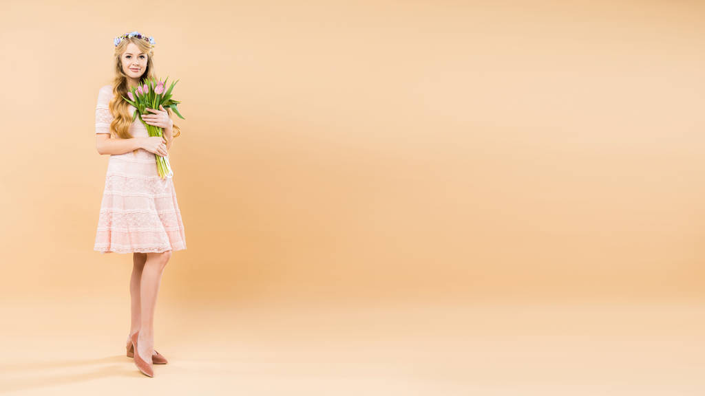 привлекательная женщина в нежном кружевном платье и цветочный венок с букетом розовых тюльпанов на желтом фоне с копировальным пространством
 - Фото, изображение
