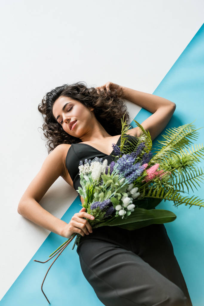 Ontspannen krullend vrouw met bloemen liggen op witte & blauwe achtergrond - Foto, afbeelding