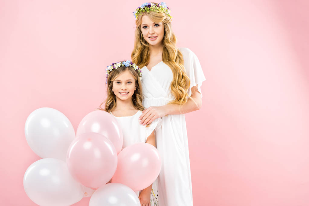 süßes lächelndes Kind mit festlichen Luftballons, die neben der schönen Mutter auf rosa Hintergrund stehen - Foto, Bild