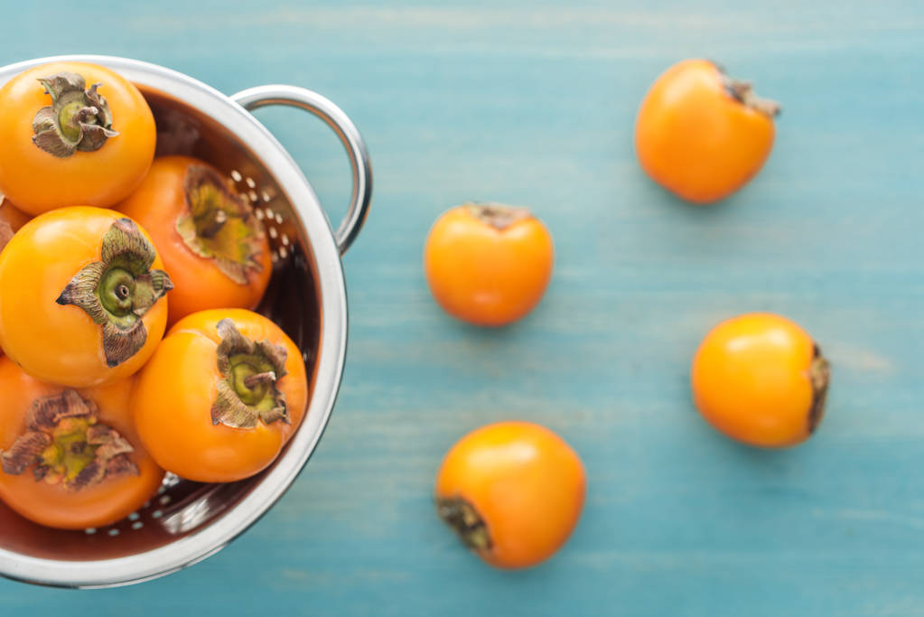selective focus of juicy orange persimmons in colander on blue background  - Photo, Image