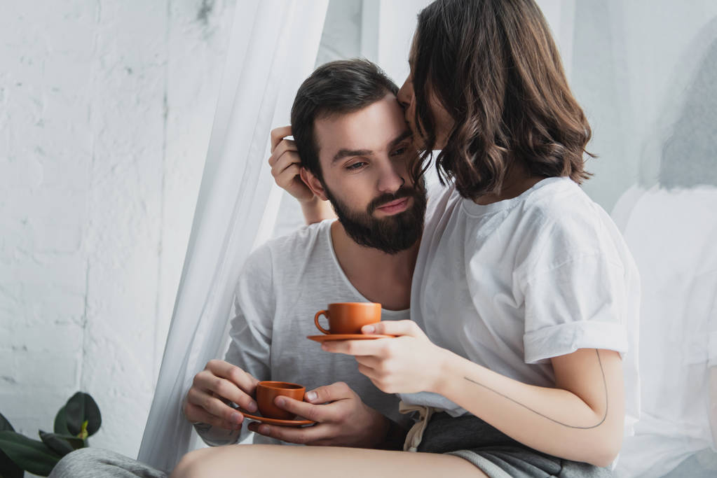 beautiful young couple kissing while having coffee at home in morning - Photo, Image