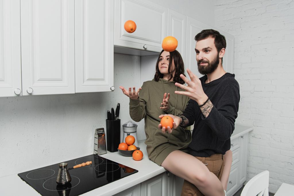 mooie jonge paar plezier en jongleren met sinaasappelen in keuken - Foto, afbeelding
