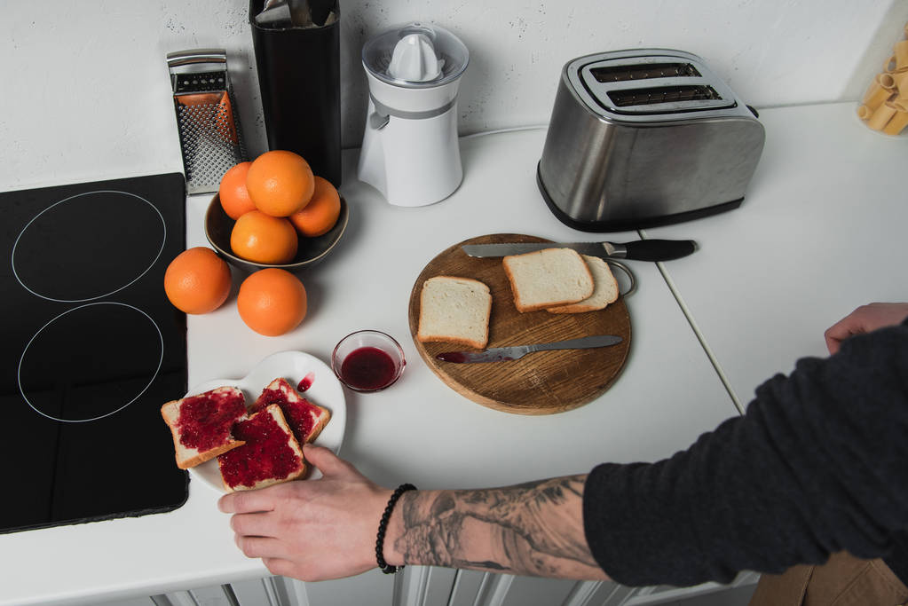 oříznutý pohled člověka připravovat toasty s marmeládou během snídaně v kuchyni - Fotografie, Obrázek