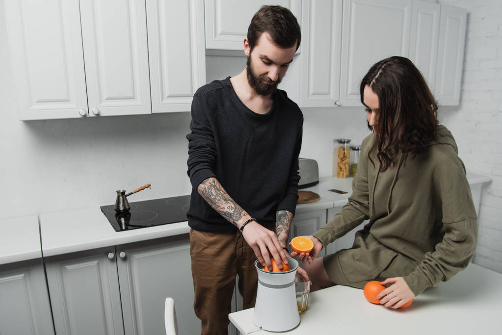 beautiful young couple preparing orange juice during breakfast in kitchen - Photo, Image