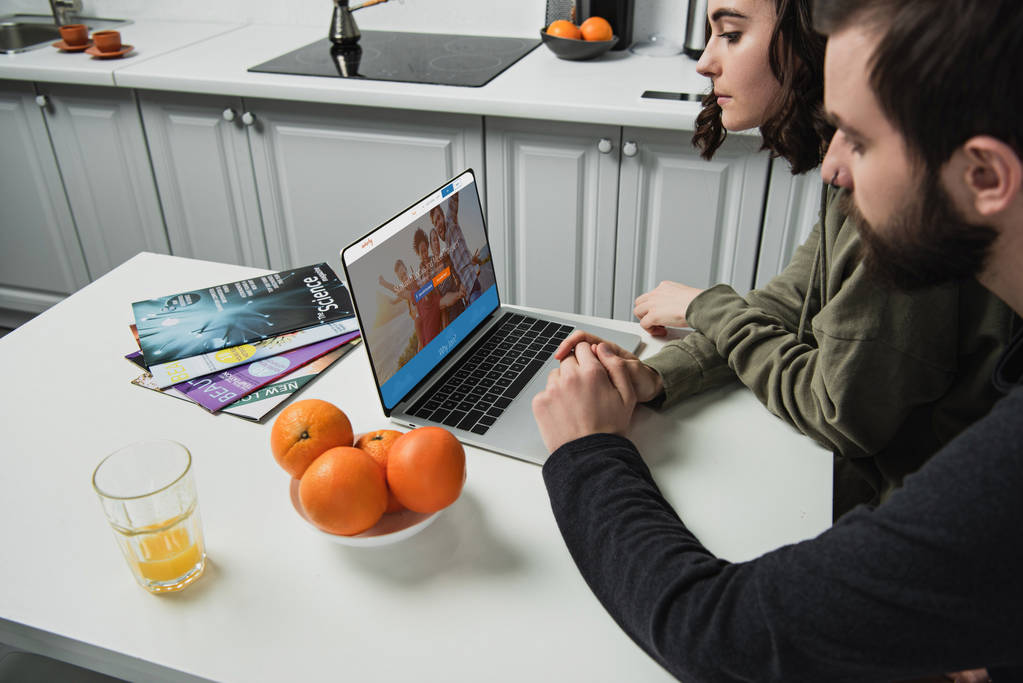 para siedzi przy stole i za pomocą laptopa z couchsurfing witryny na ekranie w kuchni - Zdjęcie, obraz