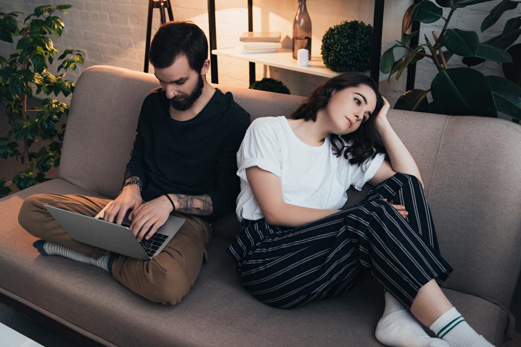 bored woman sitting on couch while man using laptop in living room - Photo, Image