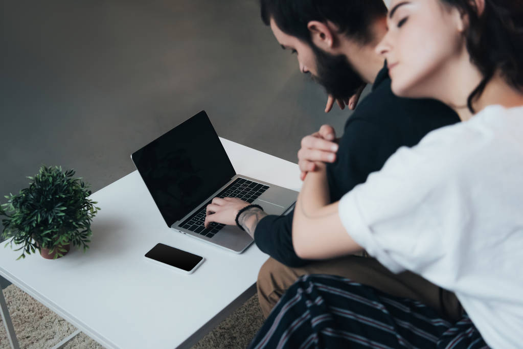 pareja sentada ang abrazos mientras se utiliza el ordenador portátil con pantalla en blanco en casa
  - Foto, imagen