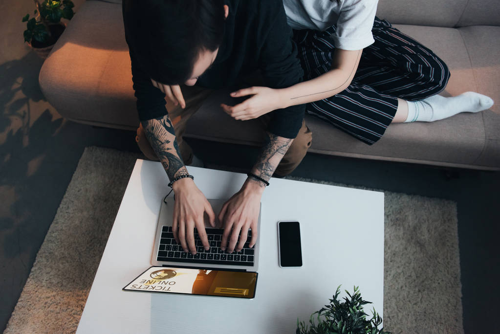 abgeschnittene Ansicht von Paar sitzt ang Umarmung, während mit Laptop mit Tickets Online-Website auf dem Bildschirm zu Hause  - Foto, Bild