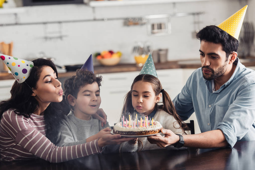 Szczęśliwa rodzina hiszpanin partii CAPS dmuchanie na świeczki na tort urodzinowy w domu - Zdjęcie, obraz