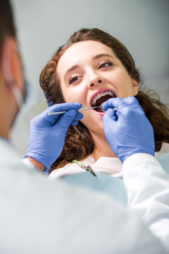 selective focus of attractive woman in braces during examination of teeth near dentist - Photo, Image