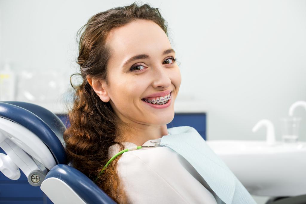 щаслива жінка в брекетах посміхається під час огляду в стоматологічній клініці
 - Фото, зображення