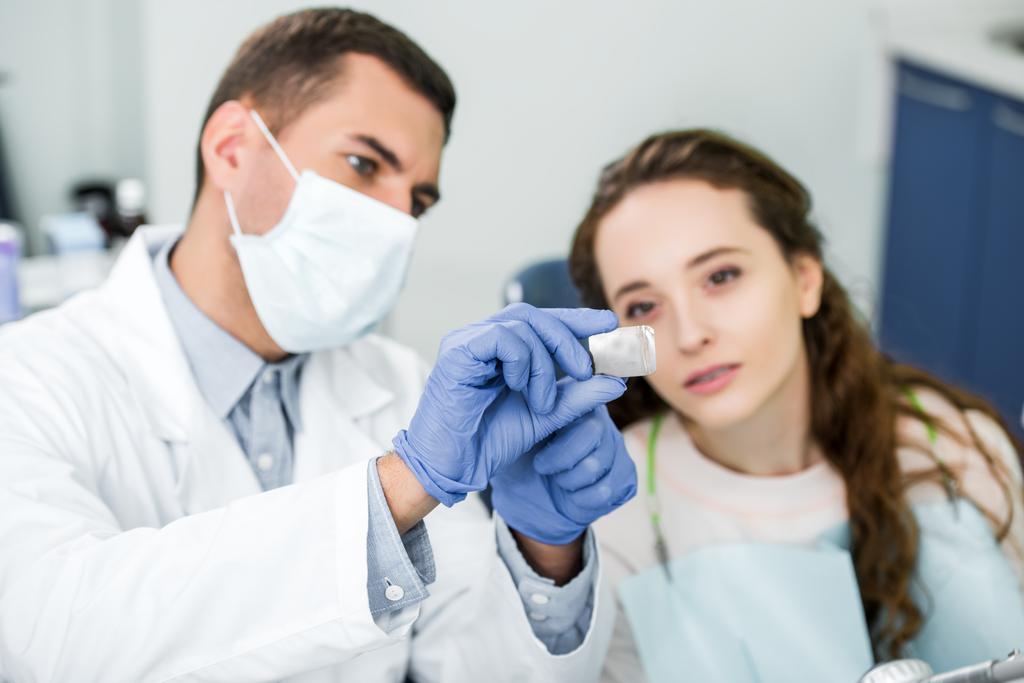 επιλεκτική εστίαση των ακτίνων χ των δοντιών στα χέρια του ο οδοντίατρος στο λάτεξ γάντια και μάσκα κοντά σε ασθενή - Φωτογραφία, εικόνα