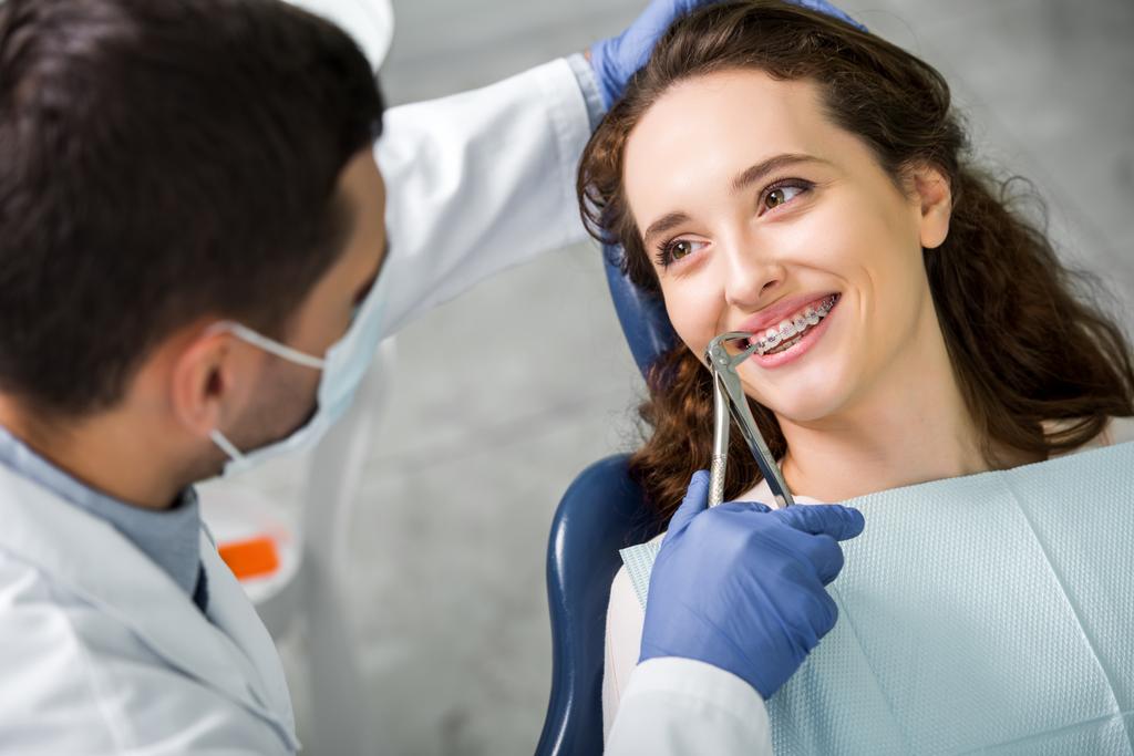 selective focus of woman smiling while looking at dentist during examination  - Photo, Image