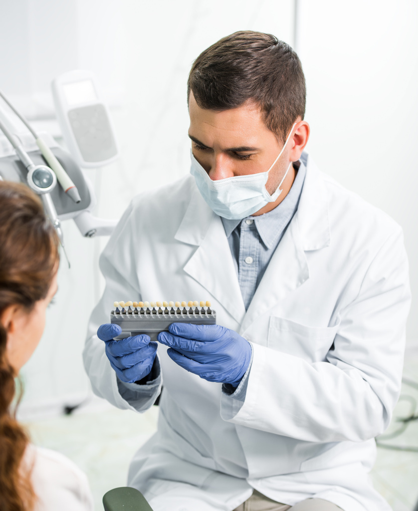 женщина выбирает цвет зубов рядом с стоматологом в маске и латексных перчатках
 - Фото, изображение