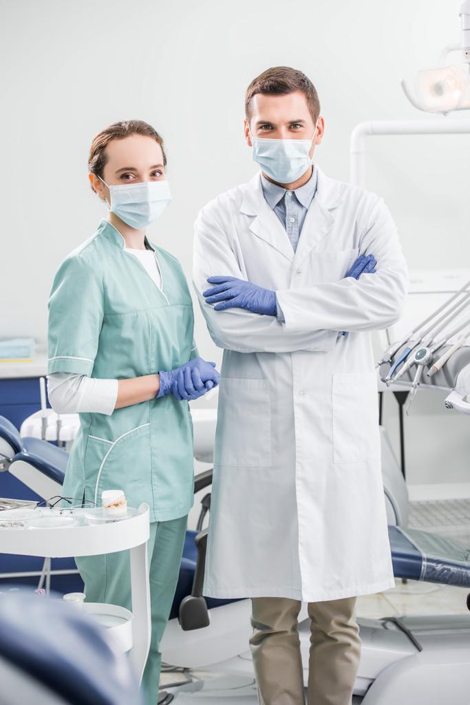 selectieve aandacht van tandartsen in maskers permanent met gekruiste armen in tandheelkundige kliniek - Foto, afbeelding