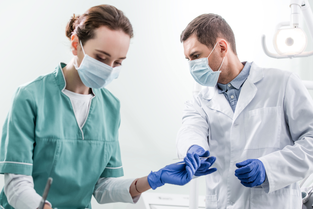 male dentist giving dental instrument to female colleague in mask - Photo, Image