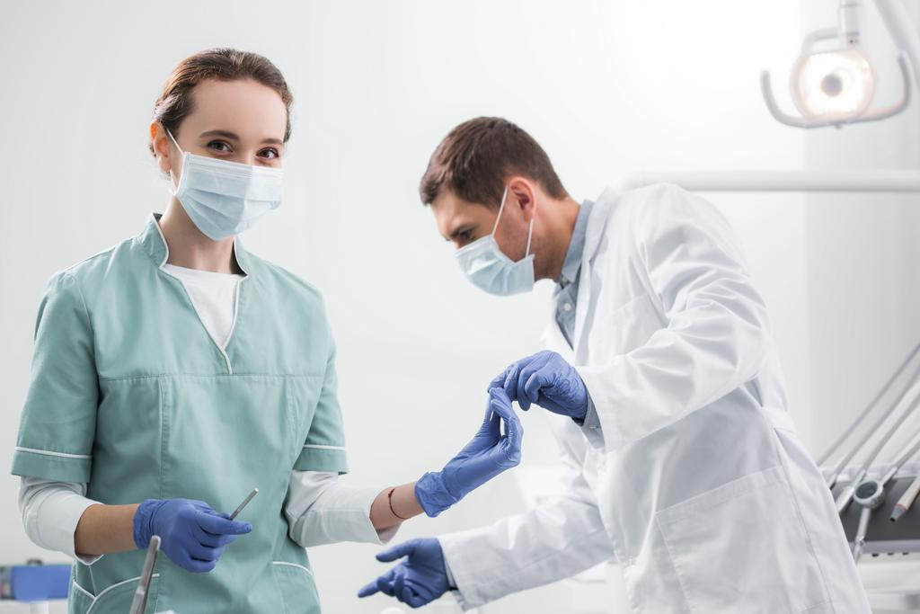  стоматолог, дающий стоматологический инструмент женщине-коллеге в маске
 - Фото, изображение