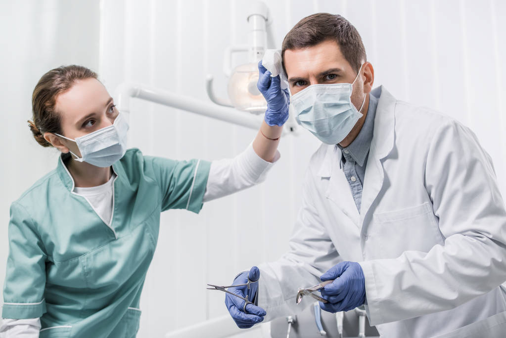歯科用器具を保持している同僚を見てマスクで女性歯科医  - 写真・画像