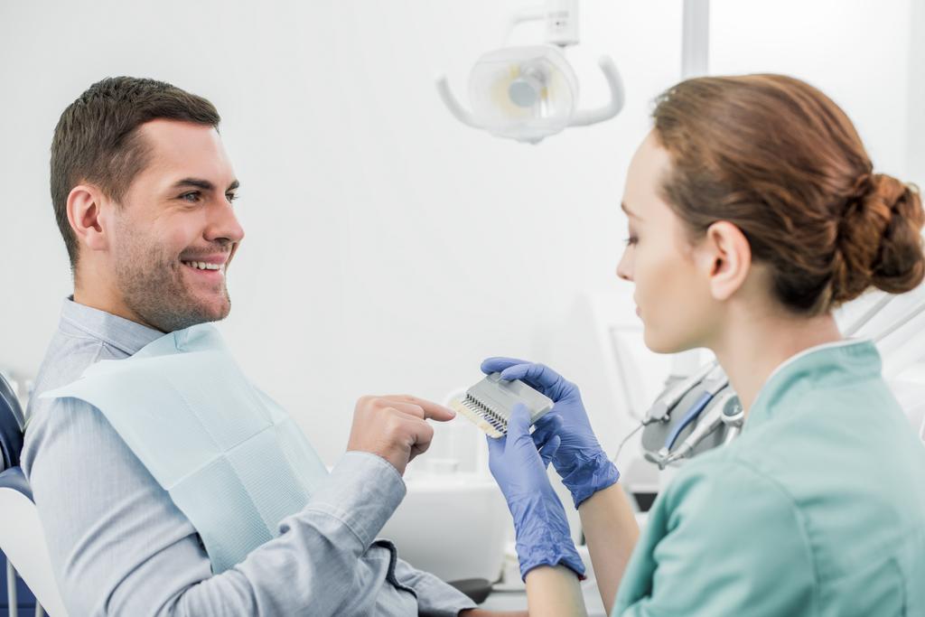 happy man pointing with finger at teeth color palette in hands of dentist - Photo, Image
