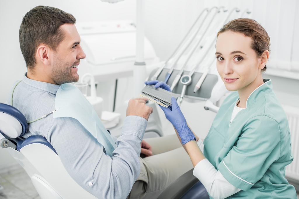 patient heureux pointant du doigt la palette de couleurs des dents près du dentiste
   - Photo, image